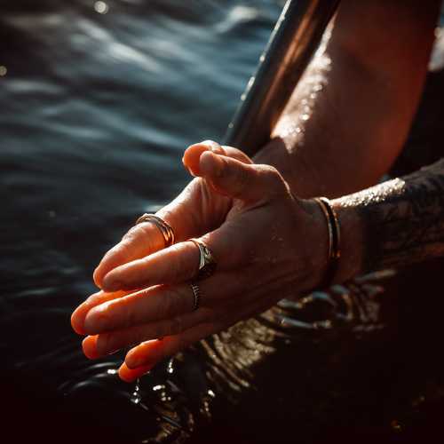 Foldede hænder med smykker over vand.