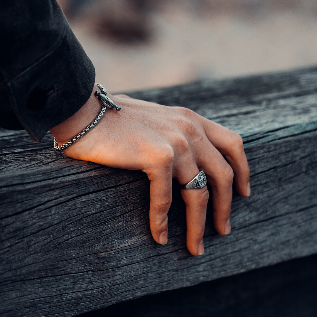 Hand resting on a wooden plank. The hand is wearing a silver ring and bracelet from Northern Legacy.